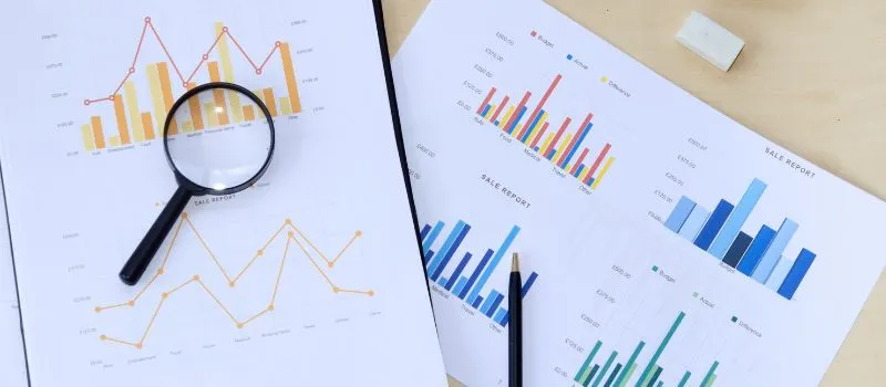 Magnifying glass and pen over printed sales report charts with bar and line graphs