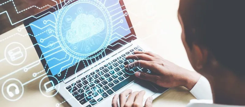 Person typing on a laptop overlaid with a glowing cloud and circuit graphic representing cloud data management