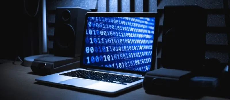 Laptop screen displaying streams of binary code in a dark room